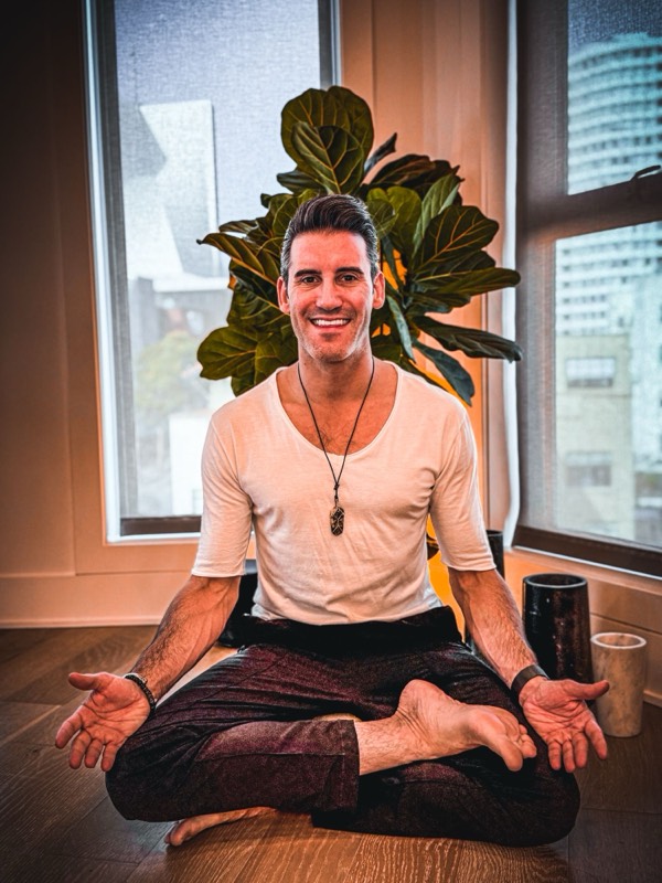 Joel sitting cross-legged on the floor, smiling, his palms open toward you